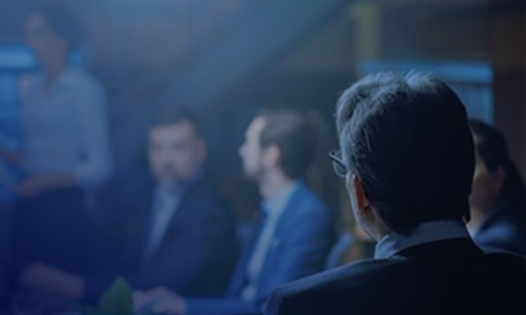 Ein Besprechungsraum mit Menschen in Geschäftskleidung, eine Person im Fokus von hinten, andere verschwommen im Gespräch.