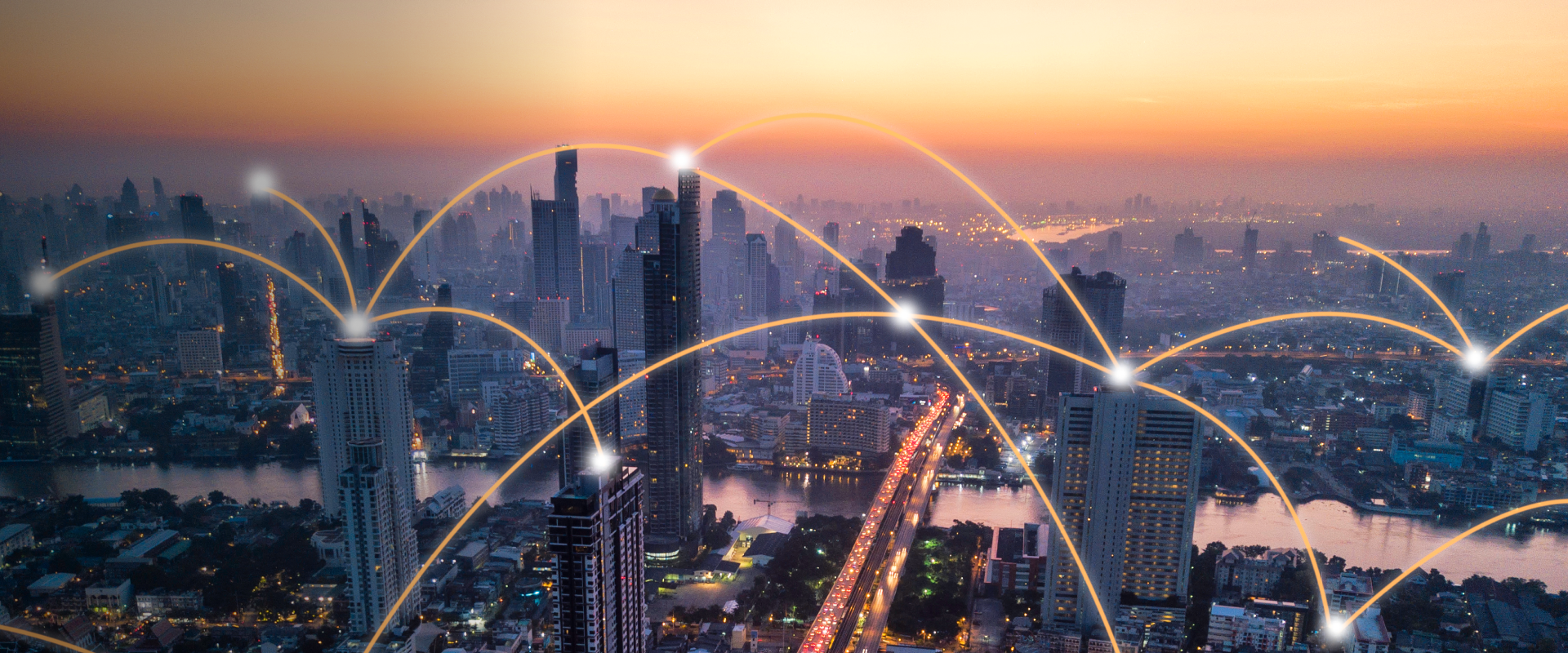 Stadtpanorama in der Dämmerung mit Wolkenkratzern, die durch leuchtende Lichtbögen miteinander verbunden sind und digitale Kommunikation und Vernetzung symbolisieren. Ein Fluss und eine Autobahn verlaufen durch die Stadt, beleuchtet von warmen Orange- und Rosatönen am Himmel.